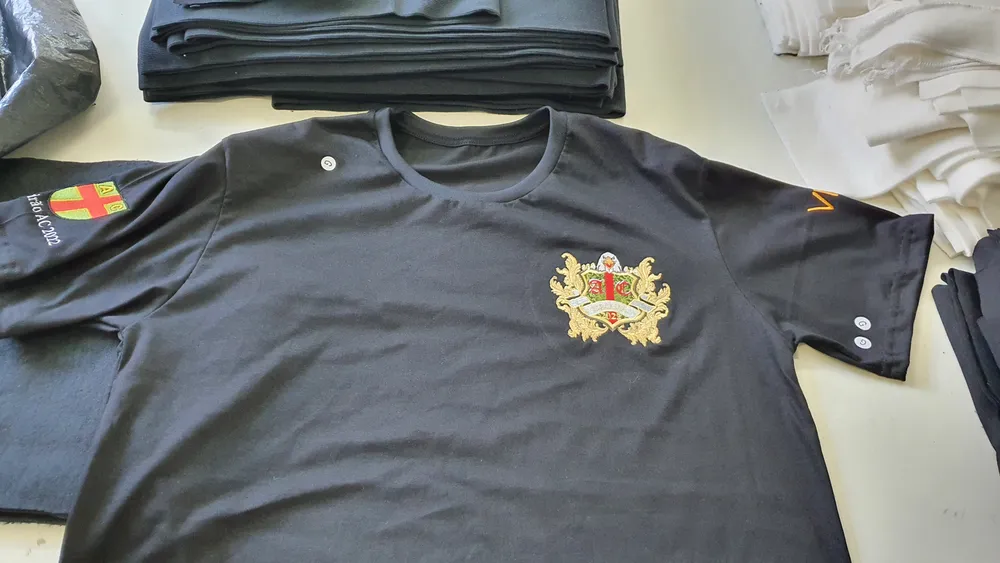 Camiseta azul marinho de turma com brasão bordado no peito e detalhe na manga