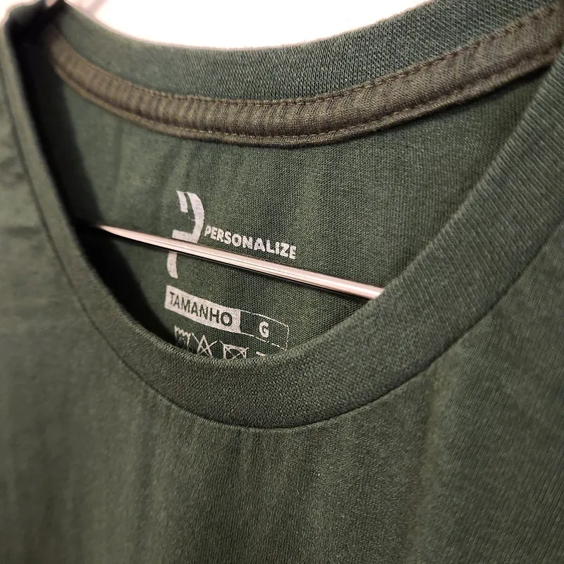 Detalhe da gola reforçada com fita ombro a ombro em camiseta verde